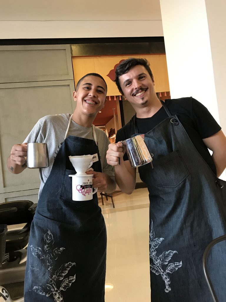 Two young baristas smiling and holding espresso pitchers